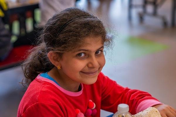 A girl smiles at the camera while eating lunch at school