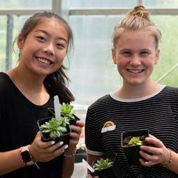 图为，两名高中生抱着温室里的小植物微笑着拍照.